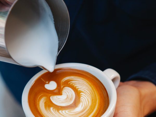 crop barista making latte art in coffee cup
