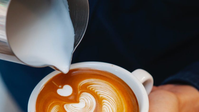 crop barista making latte art in coffee cup
